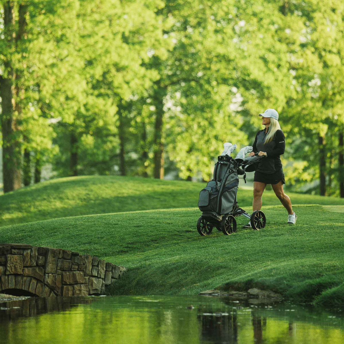 Golfer walking with a Silver/Black Bag Boy Quad Pro push cart on the golf course
