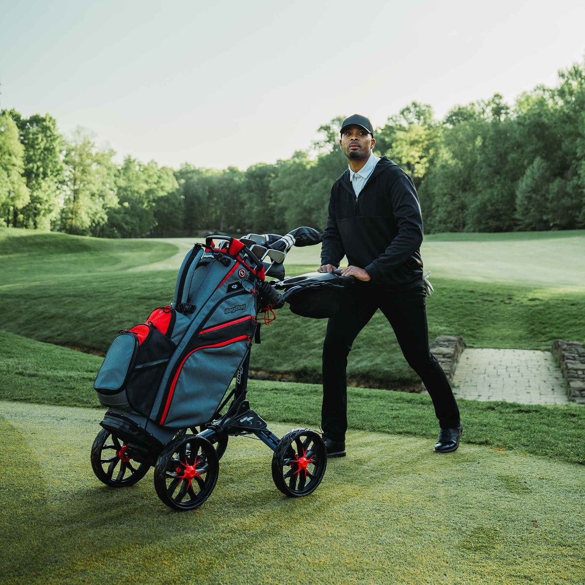 Golfer pushing a Navy/Red Bag Boy Quad Pro push cart with a golf bag on the course